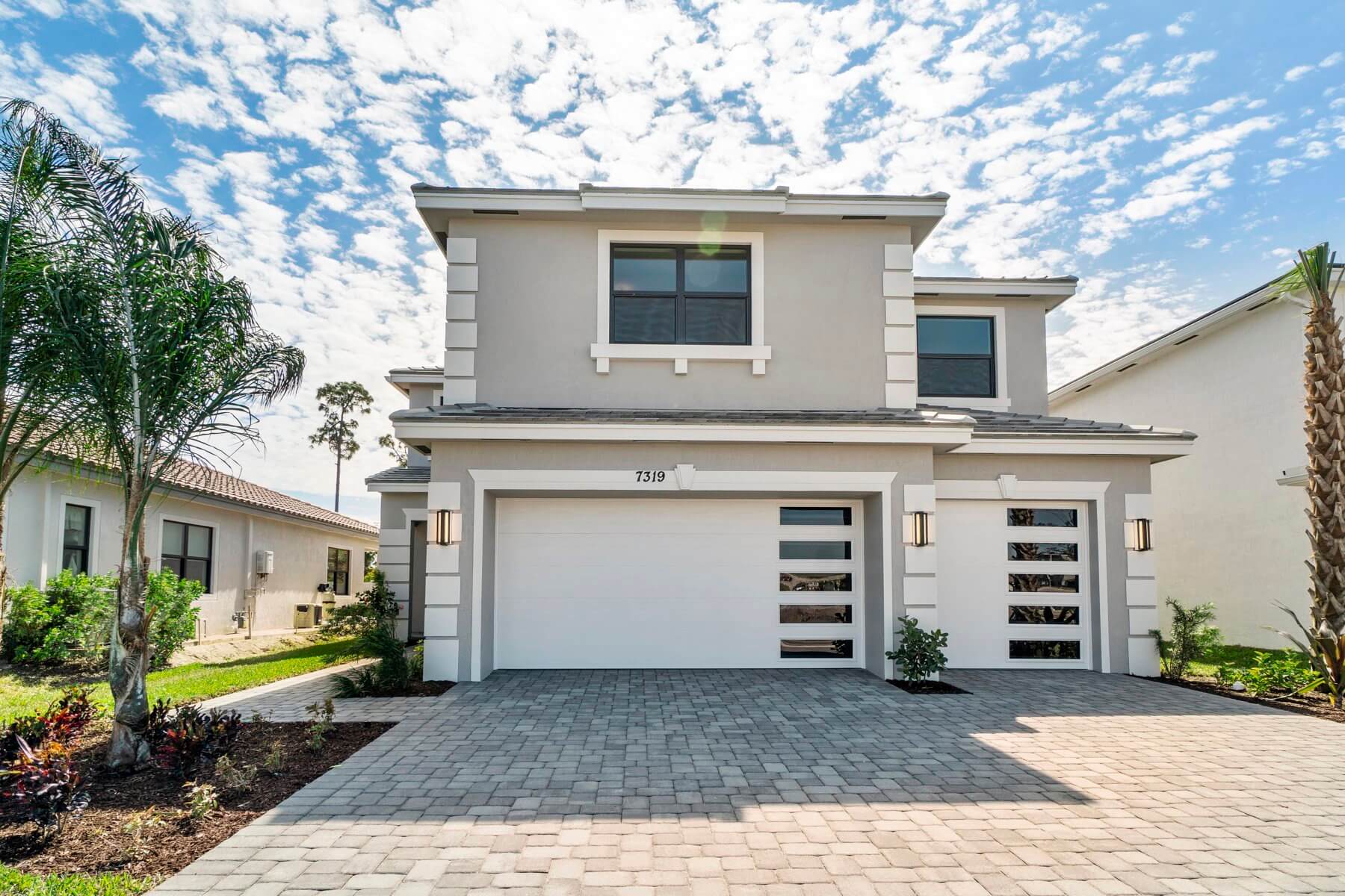 A modern two-story Akel Homes creation, this house boasts a sleek gray exterior, double garage doors, and a paved driveway, all embraced by a meticulously landscaped garden.