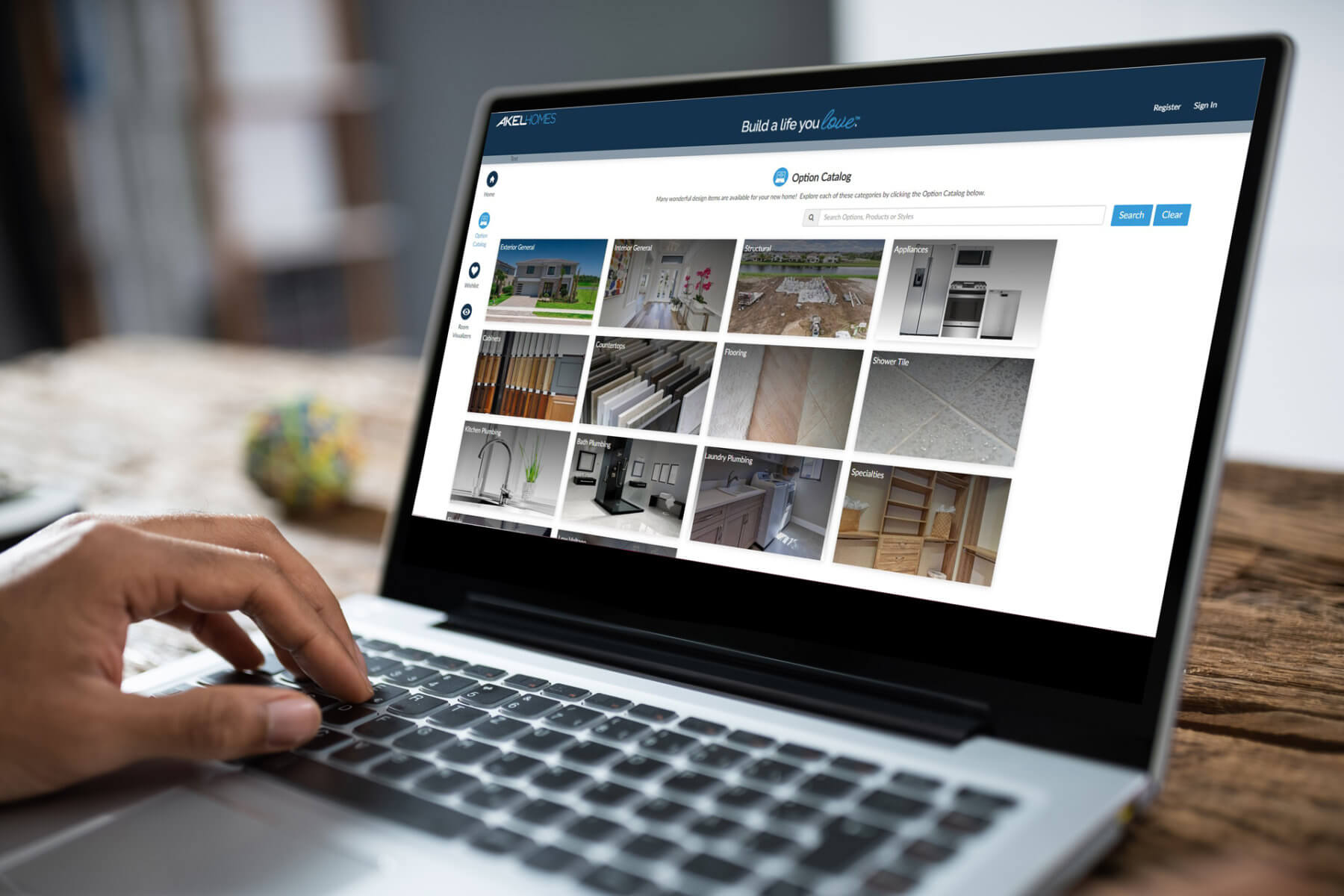 A person using a laptop to browse an online catalog from Akel Homes for home improvement products, featuring images of appliances, flooring, and cabinetry.