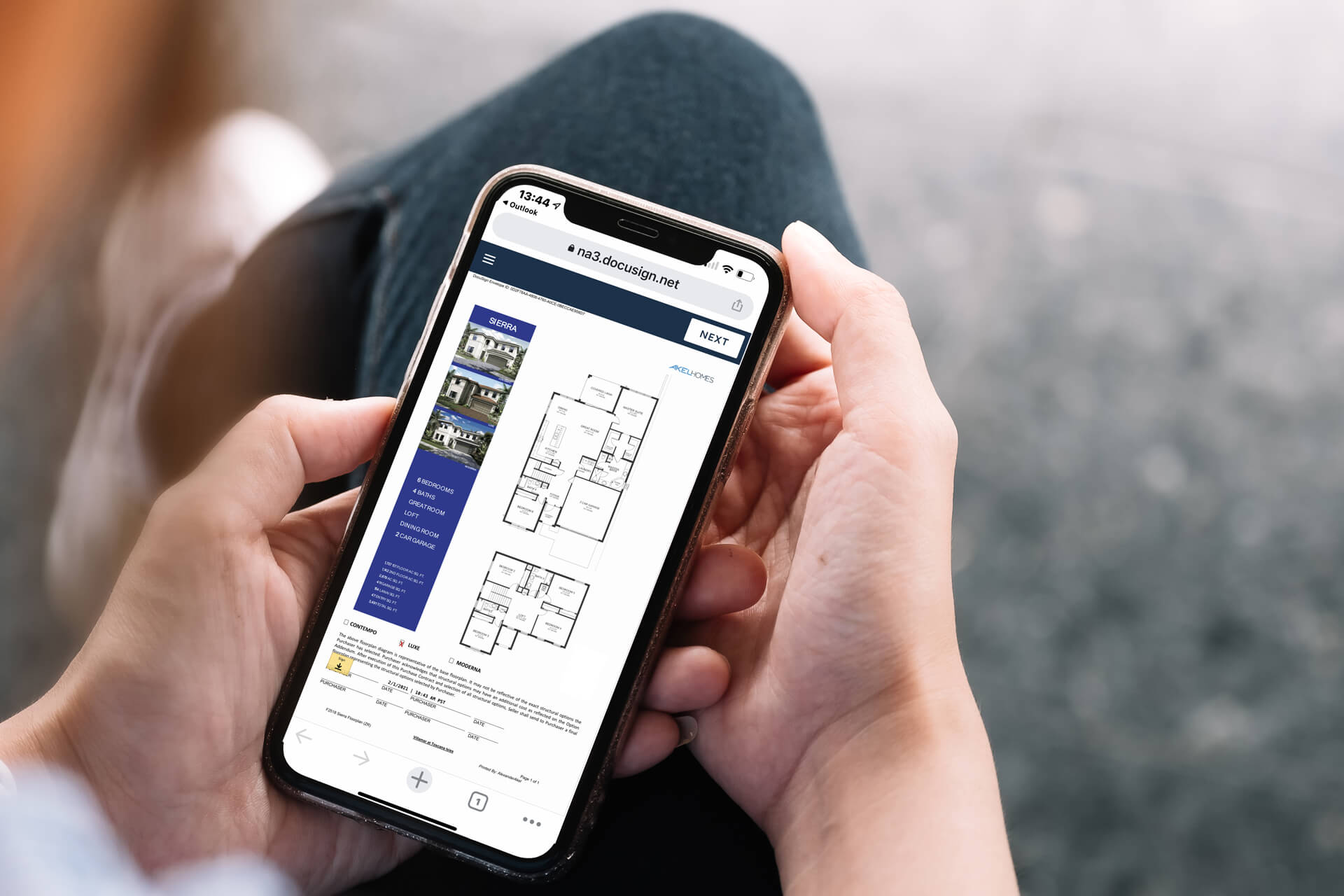 A person holds a smartphone, its screen glowing with a detailed floor plan by Akel Homes.