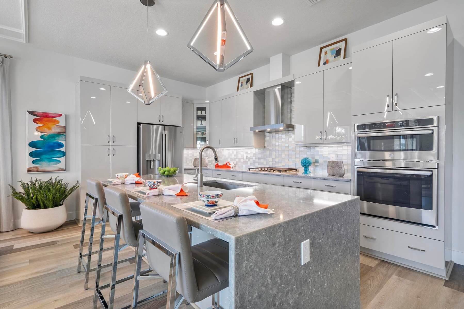 Modern kitchen by Akel Homes featuring a sleek gray island, bar stools, stainless steel appliances, pendant lights, and tasteful decorative items. The layout is bright and spacious, perfect for contemporary living.