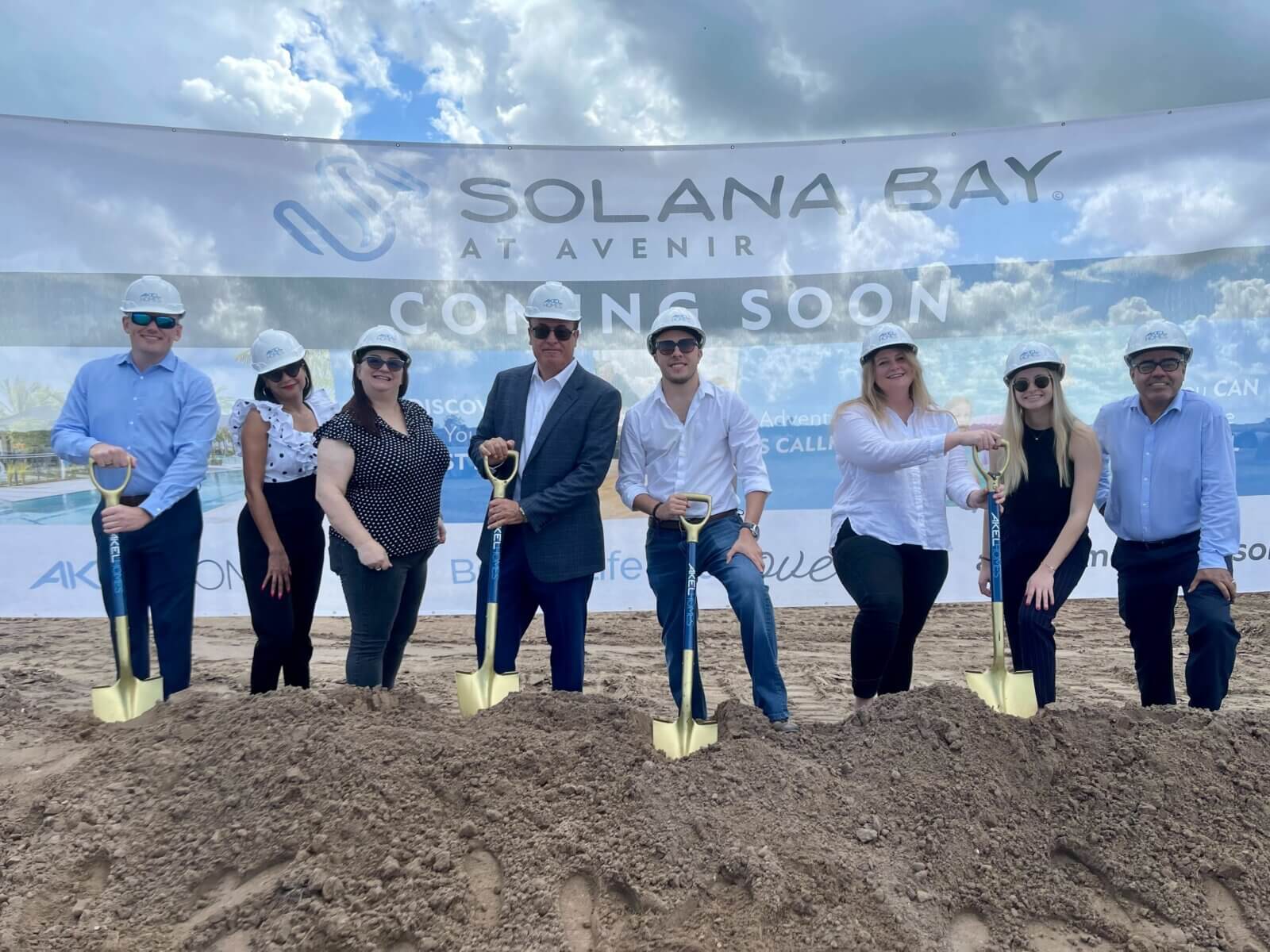 Akel Homes leads a group of people with shovels at the groundbreaking ceremony for Solana Bay at Avenir, all gathered on a dirt mound beneath a "Coming Soon" banner.