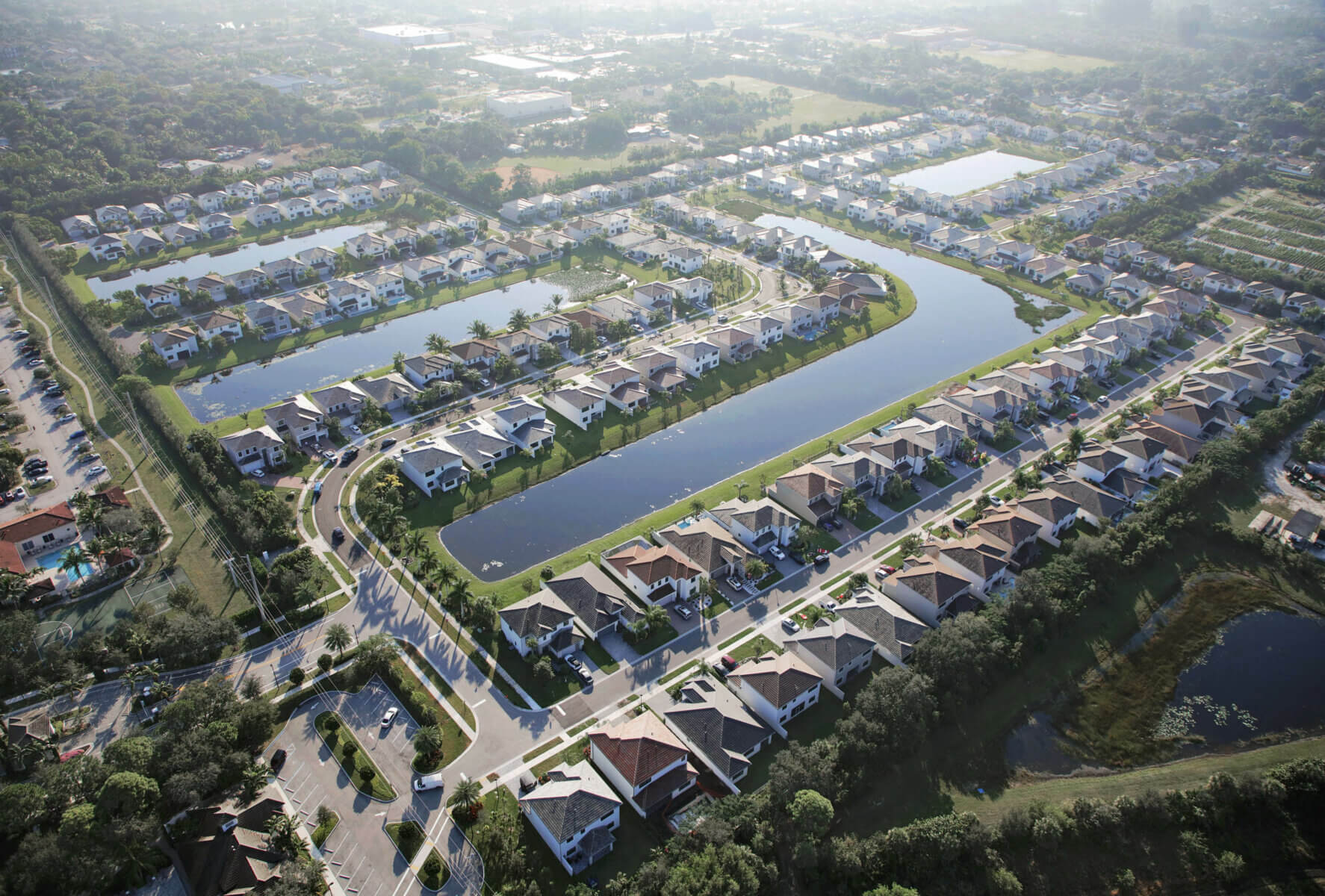 Aerial view of a suburban neighborhood by Akel Homes, featuring rows of houses, winding roads, and several rectangular ponds.