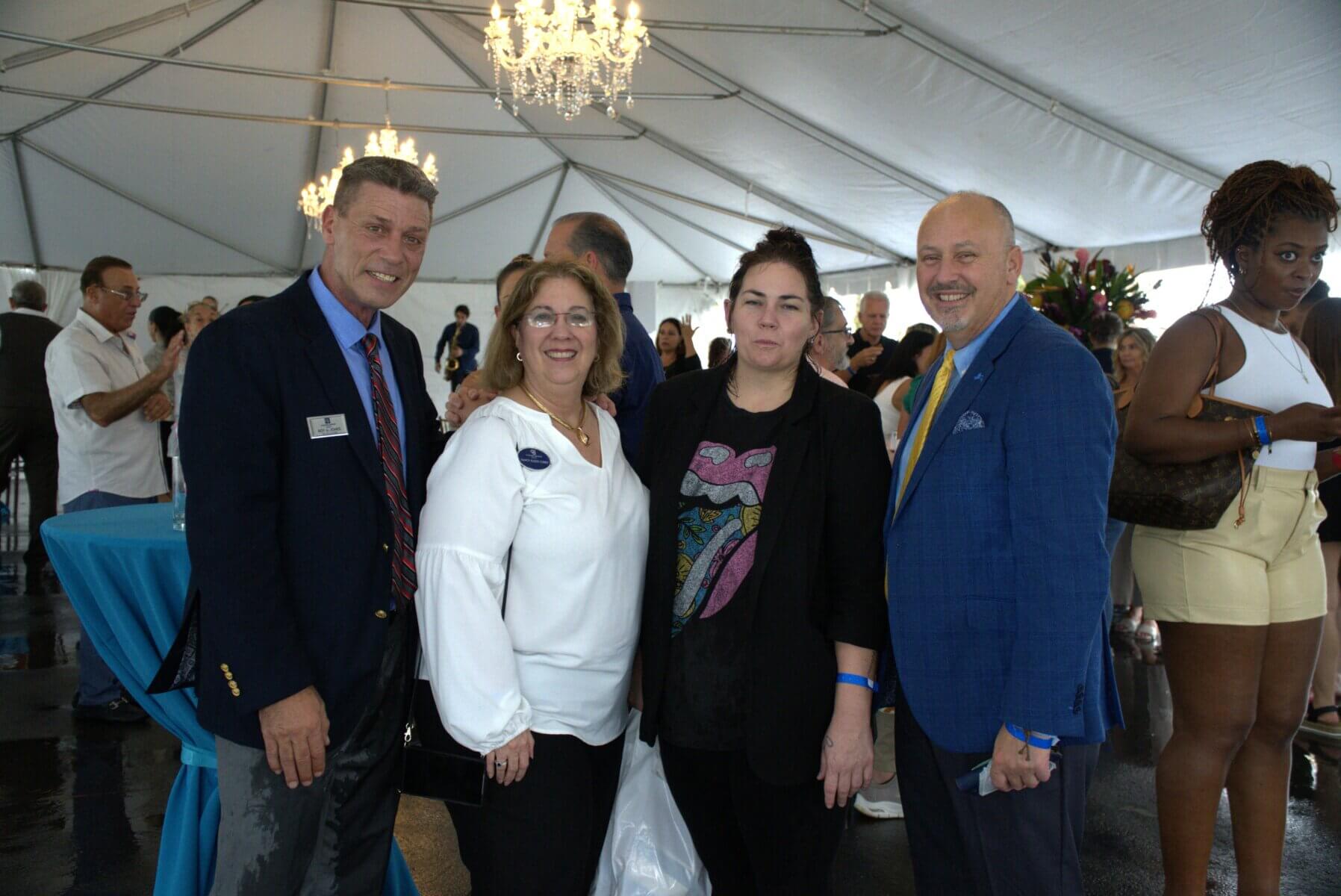 At an elegant gathering under a grand tent adorned with chandeliers, a group of people in formal attire pose with grace, reflecting the sophistication synonymous with Akel Homes.