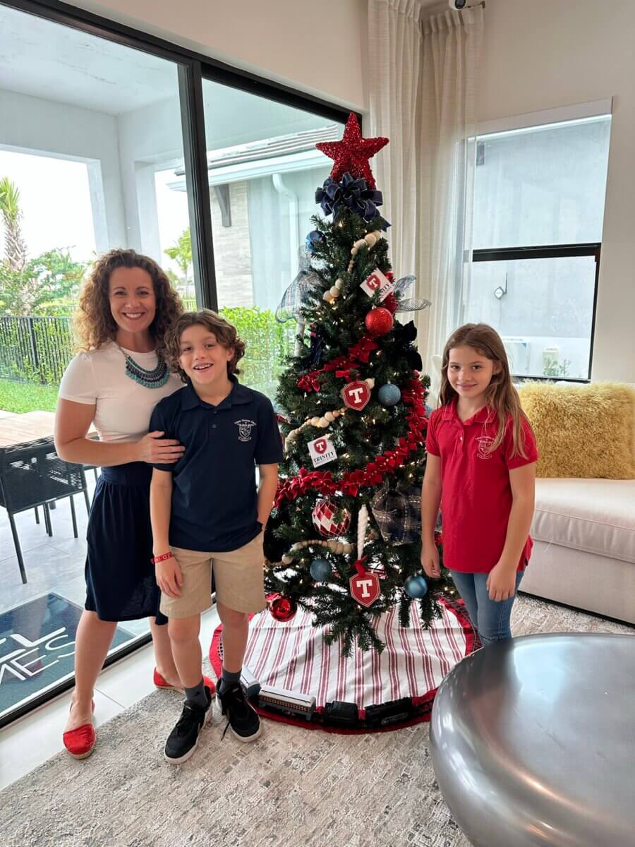 A woman and two children from an Akel Homes community stand next to a decorated Christmas tree inside a living room. The room boasts a large window with a patio view.