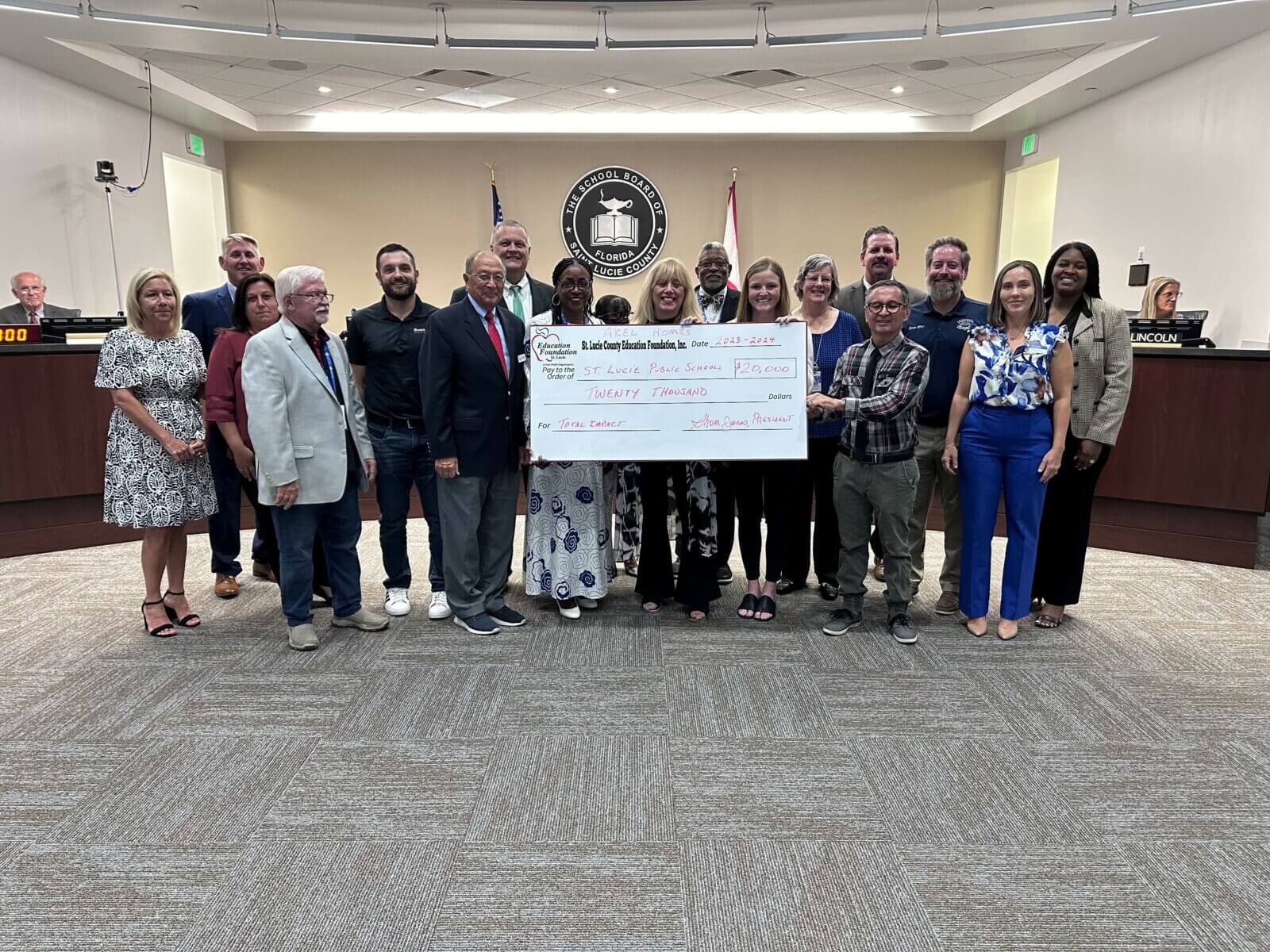 A group of people in a meeting room holds a large check reading “Safe Place FL, $30,000,” donated by Akel Homes, with officials proudly standing behind them.