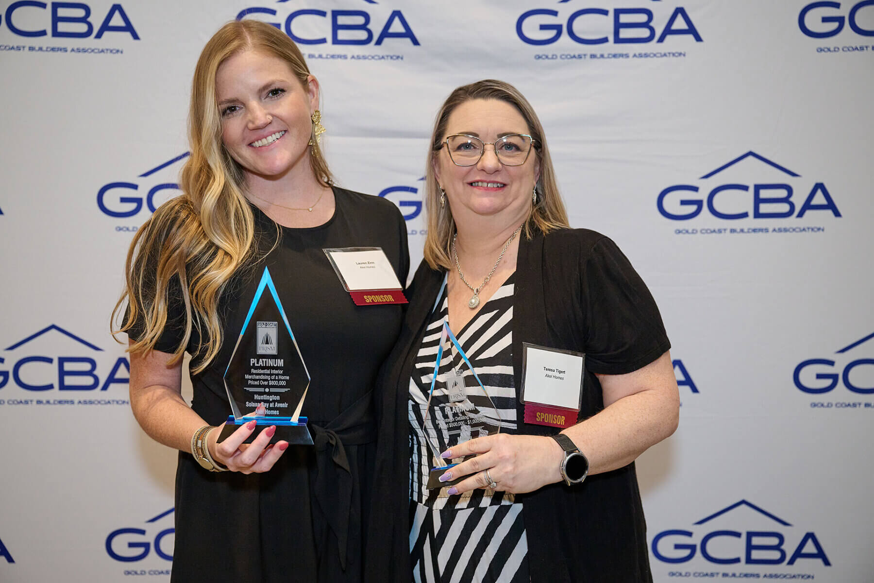 Two women proudly pose with their awards in front of a Gold Coast Builders Association backdrop, showcasing the excellence of Akel Homes.