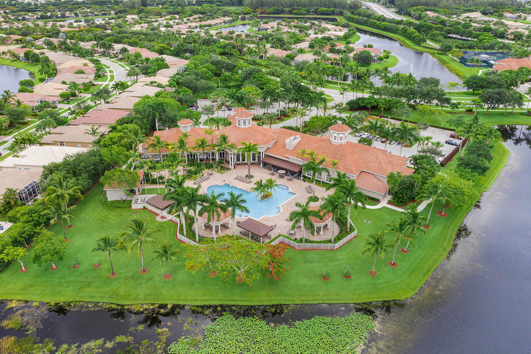Aerial view of a large, upscale residential property by Akel Homes, with a central swimming pool, lush lawns, palm trees, and water on three sides—showcasing the exceptional communities found in New Homes Construction South Florida.