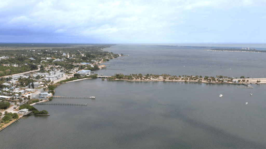 Aerial view of Catalina Palms in Port St. Lucie, a coastal town featuring houses, docks, and a bridge over calm water—an inviting setting ideal for 55+ buyers seeking serene waterfront living under a partly cloudy sky.