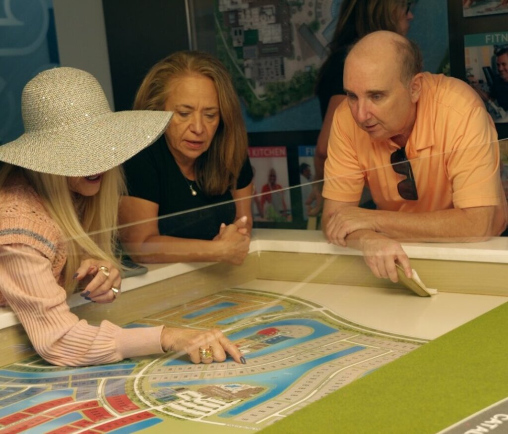 Three people closely examine and discuss a colorful architectural model layout on a table, with one person pointing to a specific area—highlighting why it pays to get in early on new projects.