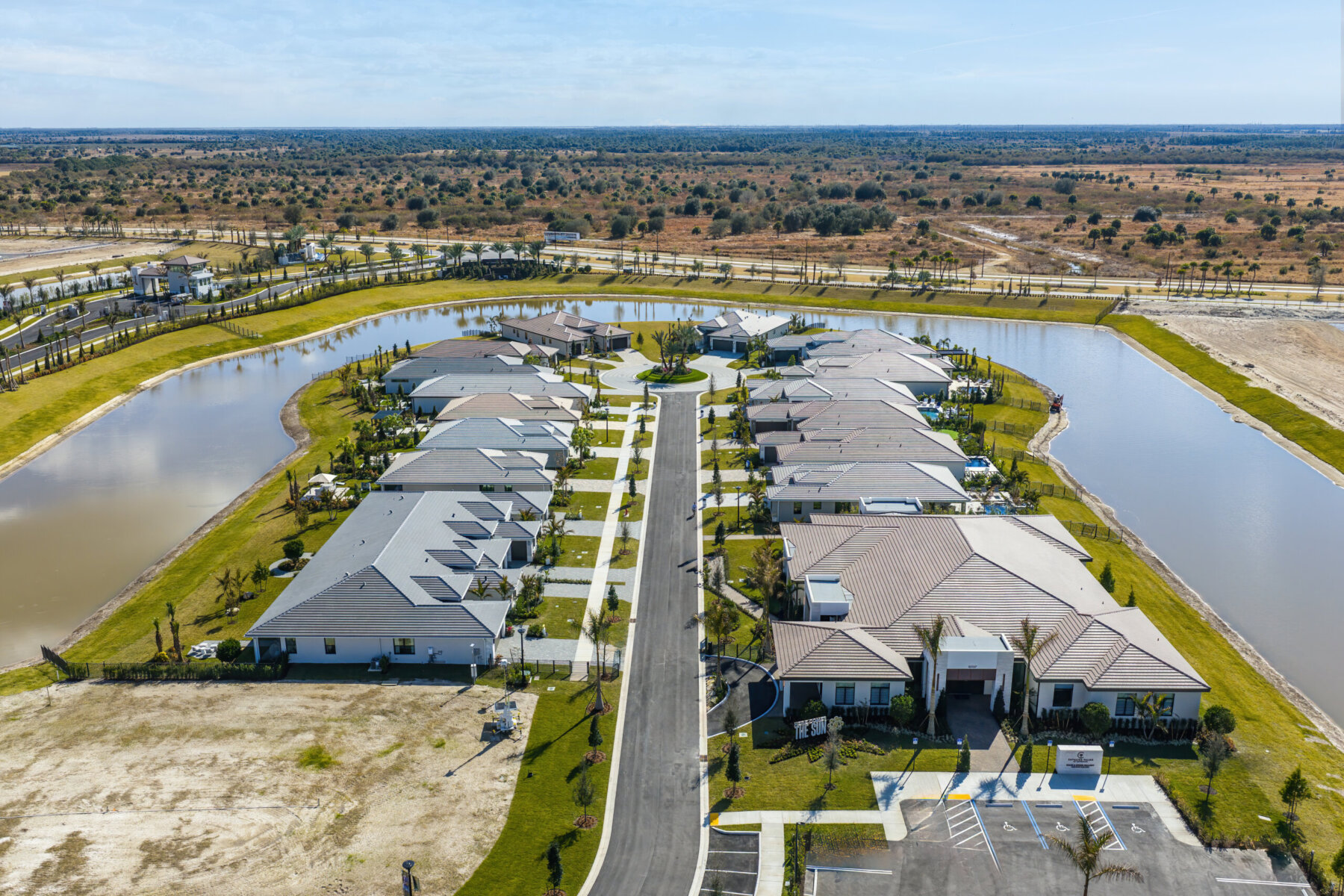 Aerial view of a suburban residential neighborhood with single-story homes arranged along a central road, surrounded by water features and open land.
