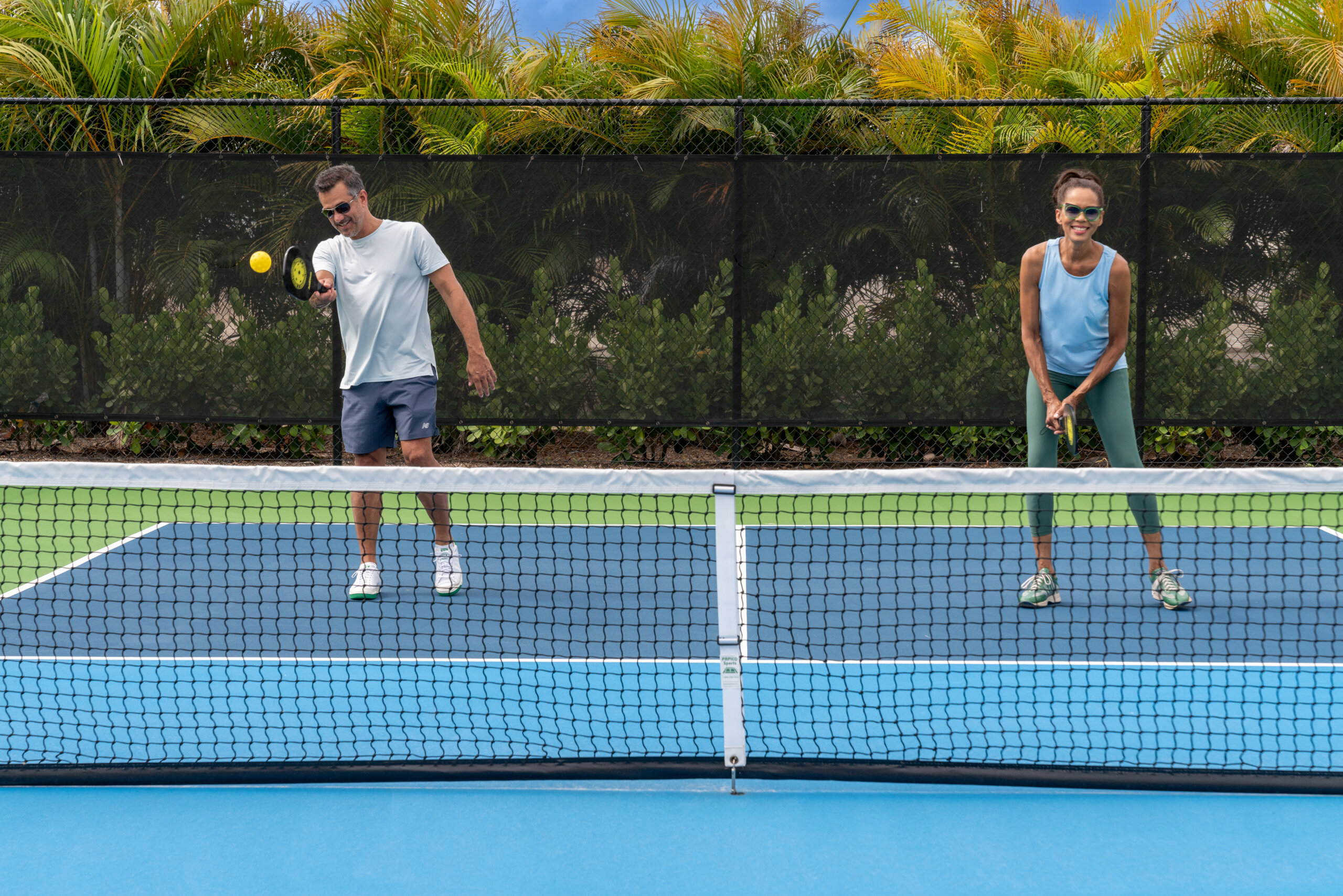Four adults in a swimming pool participate in a water aerobics class, lifting foam dumbbells above their heads near the pool edge, enjoying an energizing Catalina Palms experience.