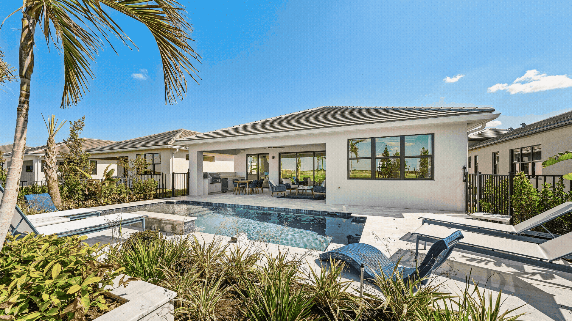 Modern house with a backyard pool, lounge chairs, covered patio, and landscaped plants under a clear blue sky.