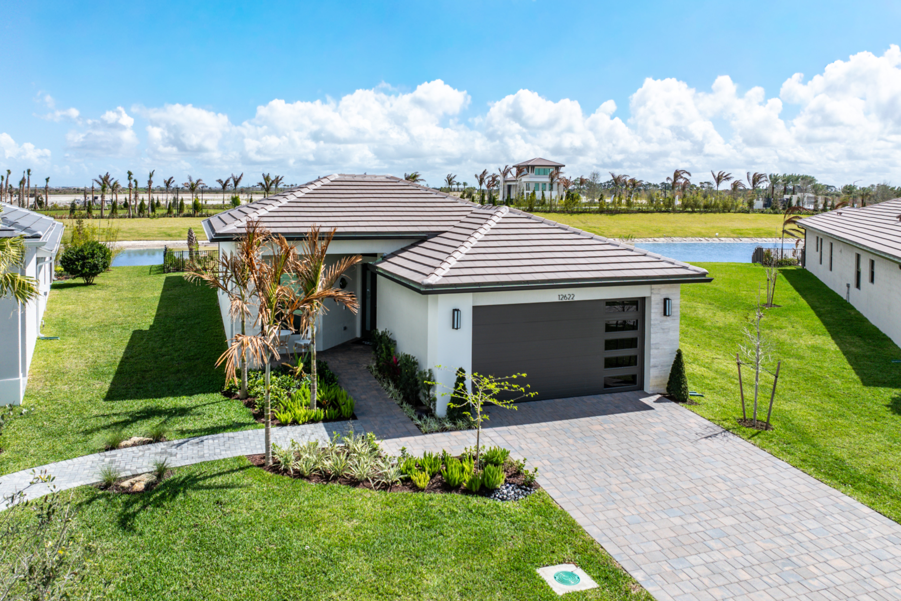 Single-story modern house at Catalina Palms with a two-car garage, light exterior, and landscaped front yard—perfect for the Sundance Homesite Preview Event in a suburban neighborhood with blue sky and palm trees.