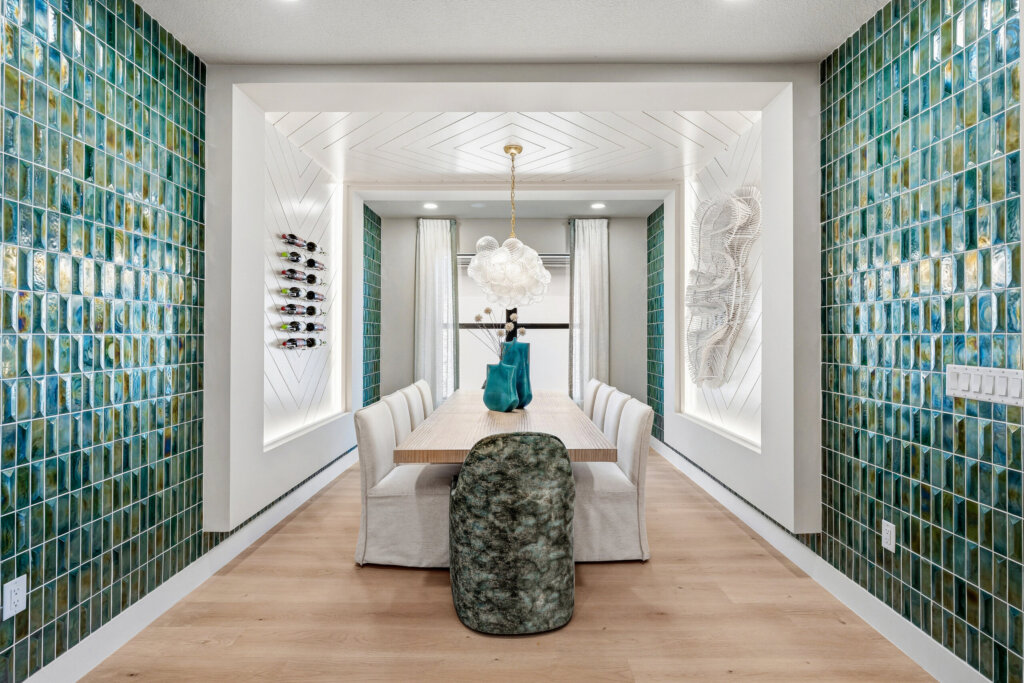 Modern dining room with green tiled walls, a long wooden table, white chairs, decorative lighting, and a large window at the far end—perfect for those who appreciate Signature Home designs like The Palm.