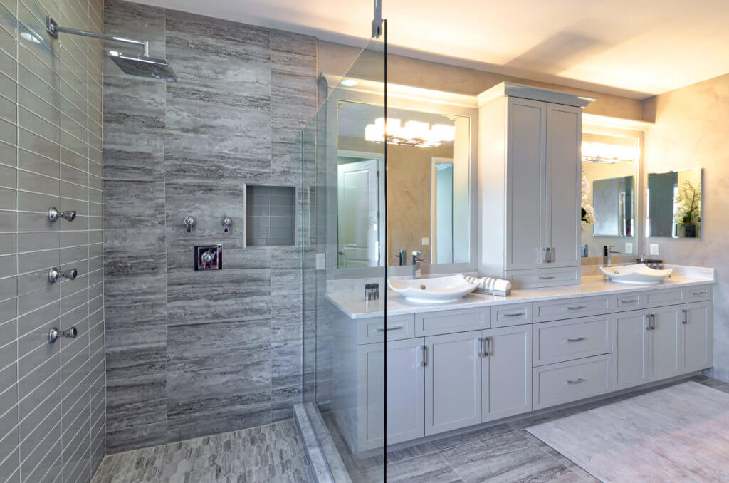 Experience the Villamar at Toscana Isles' modern bathroom, complete with a spacious glass-enclosed shower featuring dual showerheads. Enjoy a large vanity with dual sinks, ample cabinetry, and a wall-mounted mirror, all enhanced by neutral-colored tiles in a bright, well-lit ambiance.