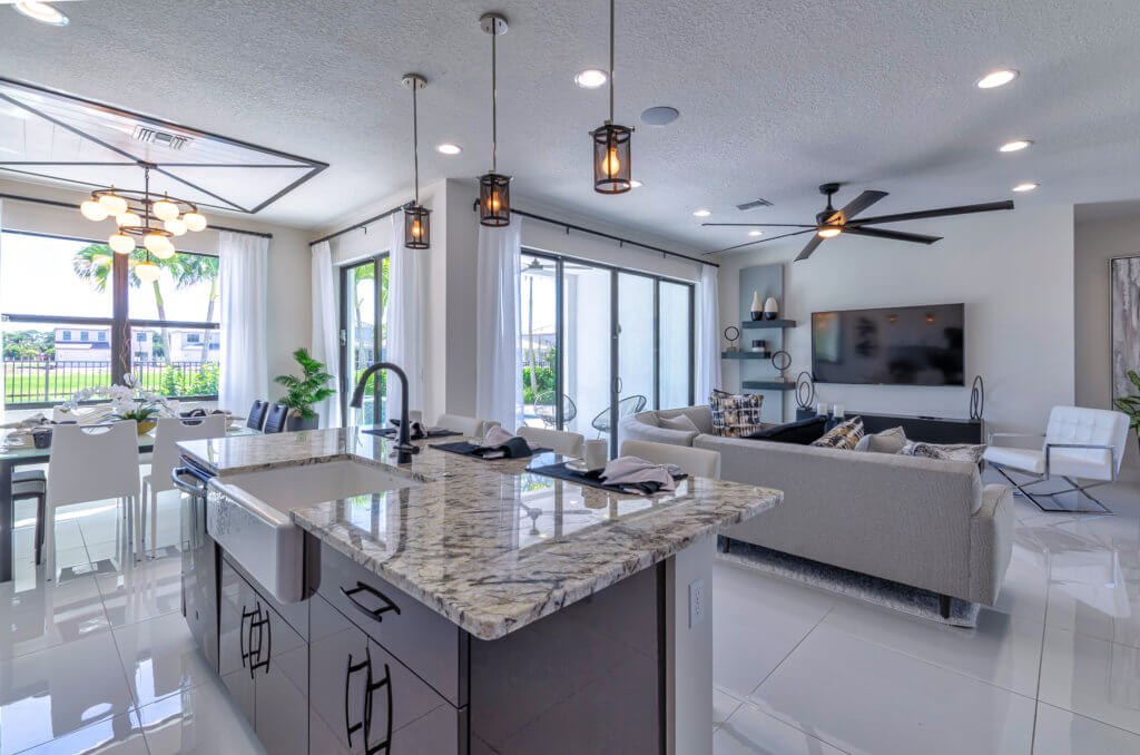 Experience luxurious living at Villamar at Toscana Isles, where a modern, open-concept space awaits. Enjoy a kitchen with a marble island and sleek black fixtures alongside the dining area and living room. Relax on light-colored sofas while natural light pours in through large windows.