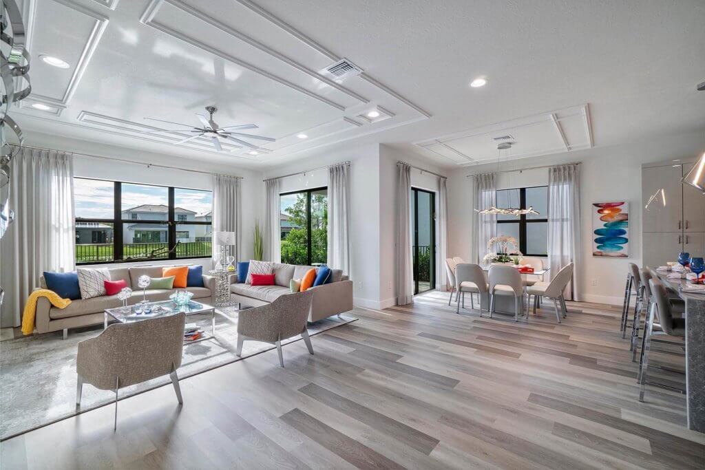 Experience the contemporary elegance of Villamar at Toscana Isles with a spacious, modern open-plan living and dining area. Large windows illuminate the room's sleek furniture and abstract art. With wood flooring and neutral walls, this vibrant space perfectly embodies upscale comfort.