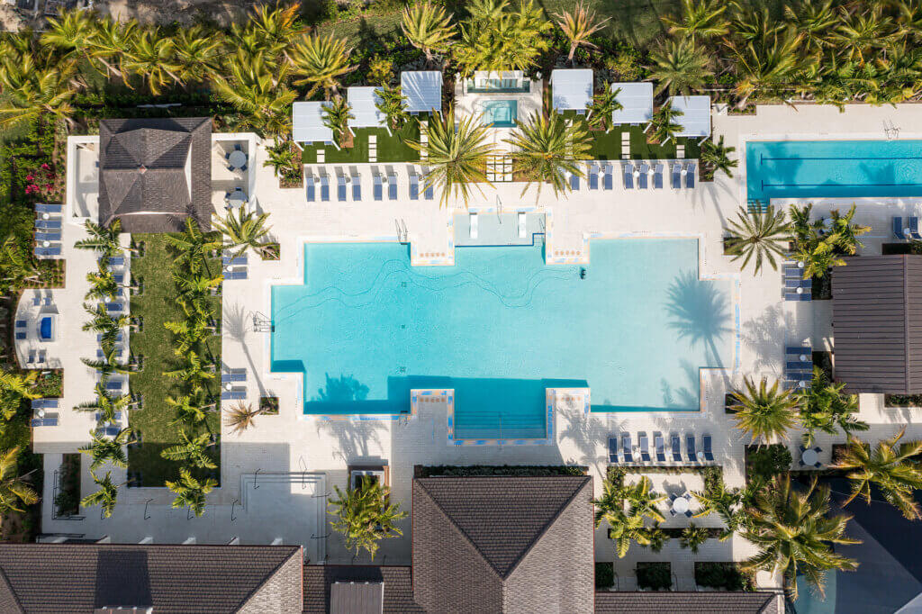 Aerial view of a rectangular outdoor swimming pool at Catalina Palms at Sundance, surrounded by lounge chairs and palm trees. The area includes a smaller rectangular pool, cabanas, and landscaped greenery, all set in a sunny, resort-like environment.