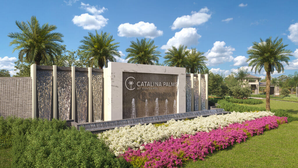 A modern monument with cascading waterfalls is flanked by tall palm trees. The structure reads "Catalina Palms." In the foreground, there are blooming magenta and white flowers. The sky is clear with a few clouds.